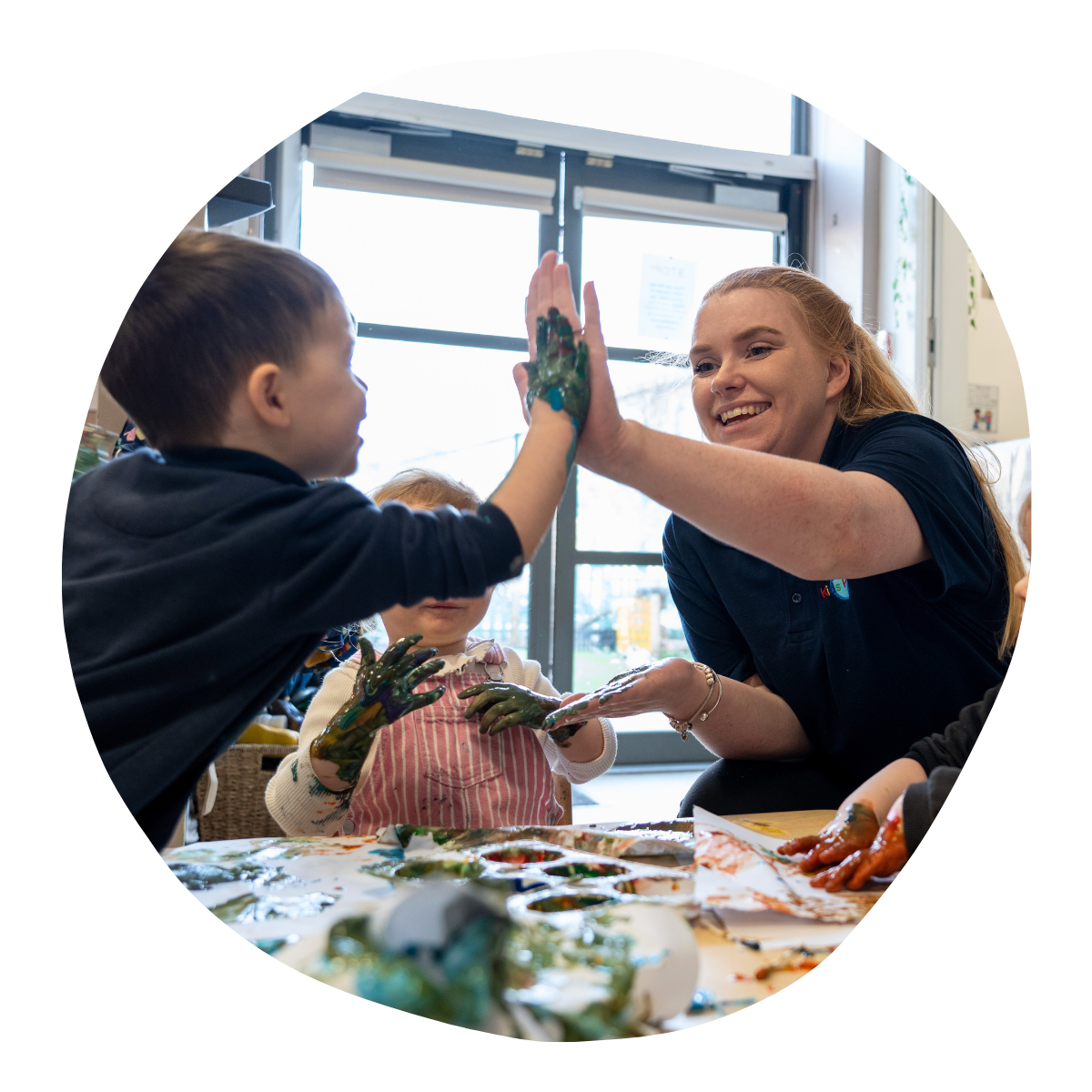 child high-fiving their key person whilst doing a painting activity