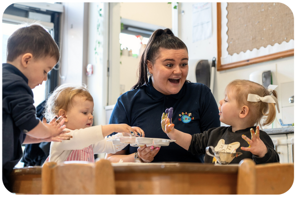 Similing nursery worker painting with three toddlers