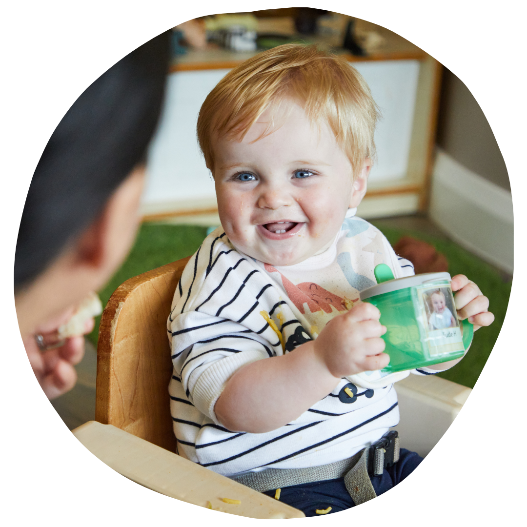 smiling baby holding cup and smiling and key nursery worker